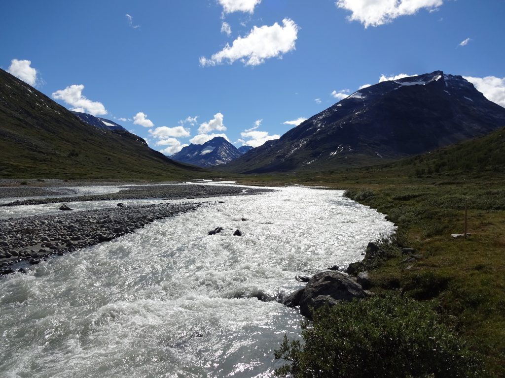 Uitzicht op helder stromend water in een dal met licht besneeuwde bergen op de achtergrond op een heldere dag met blauwe lucht en wolkjes in Noorwegen