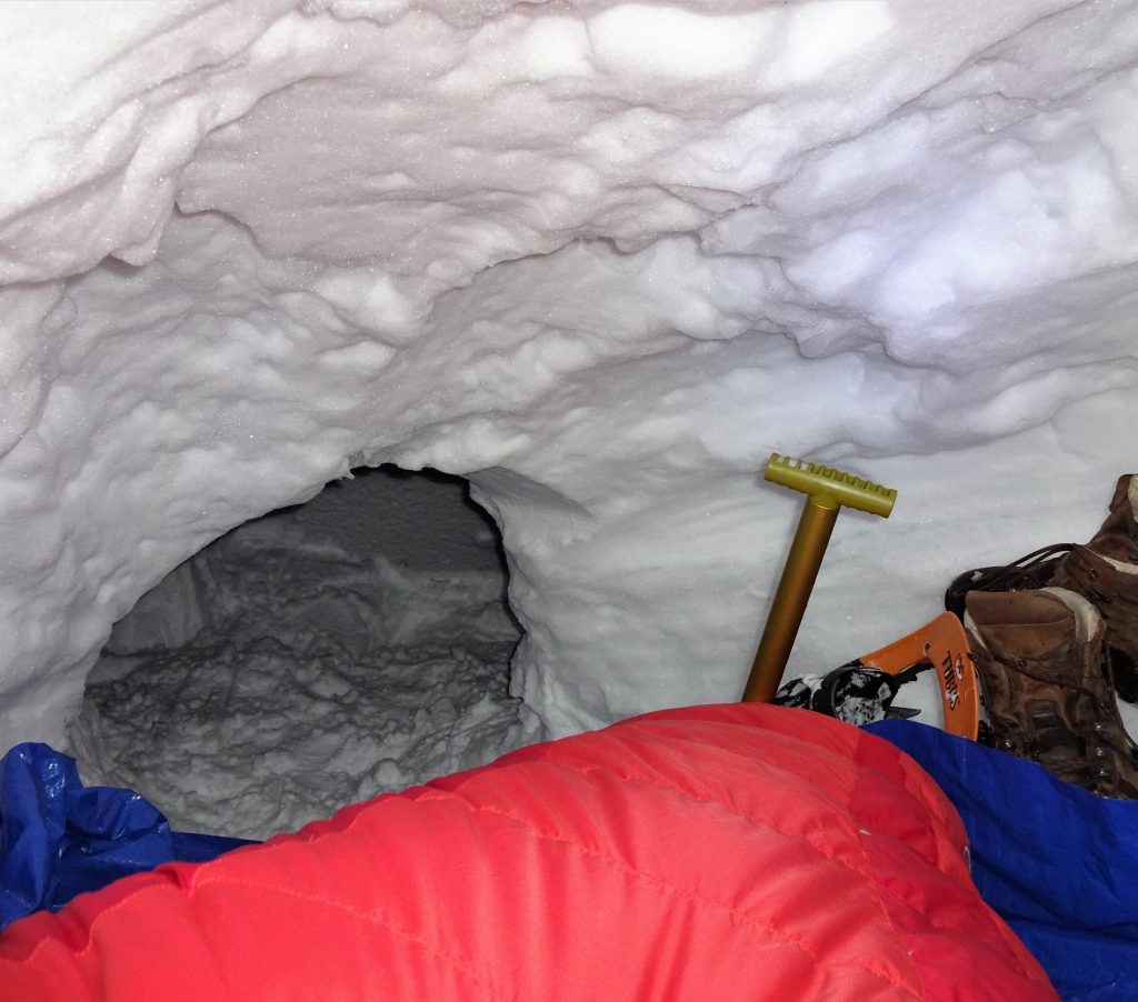 In een zelfgemaakte sneeuwhut of ook wel quinzee liggen slaapspullen, een schep, sneeuwschoenen en bergschoenen tijdens een wintertrekking in Noorwegen.