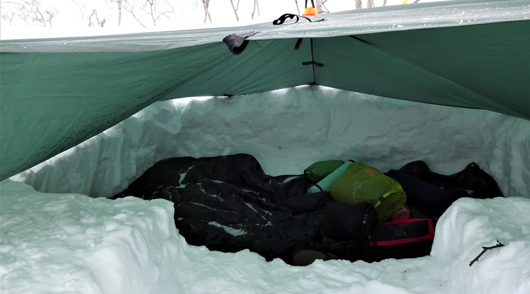 Slaapplek gegraven in de sneeuw afgedekt met een groene tarp tijdens trekking Noorwegen.