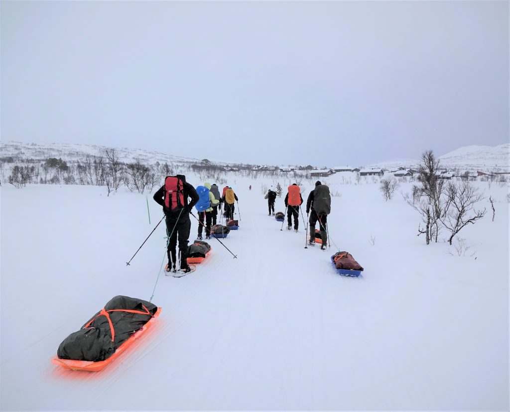 Groep cursisten loopt op sneeuwschoenen en een slede achter zich aal door het besneeuwde Noorse landschap vanwege een wintertrekking met Northern Pioneers.