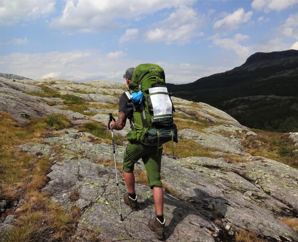 Cursist rugzaktrektocht hiked met rugzak en wandelstok over rotsachtig heuvels in het ruige berggebied in Noorwegen Setesdal.